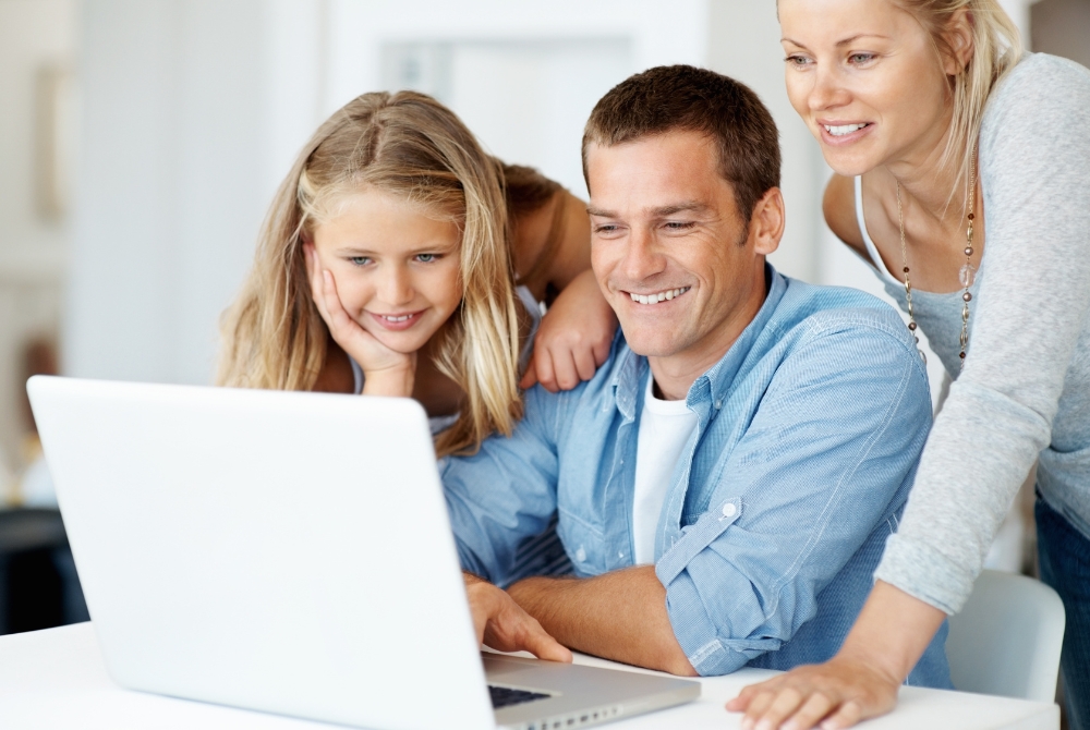 Family looking at laptop: "Happy family exploring real estate listings online in living room" — This image can be effectively used on a homepage or a blog page discussing the benefits of online house hunting or technology in real estate, targeting family-oriented buyers.